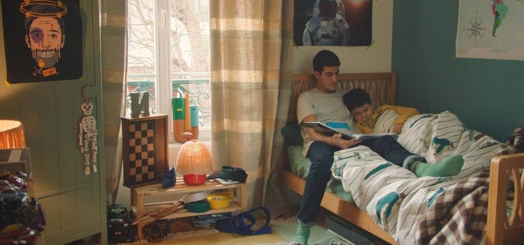 Deux frères sur un lit, le grand racontant une histoire au plus petit