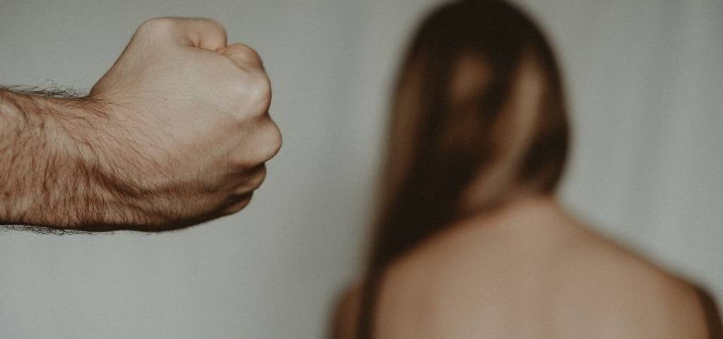 Femmes de dos face à un mur, avec un homme au 1er plan qui pointe son poingt vers elle