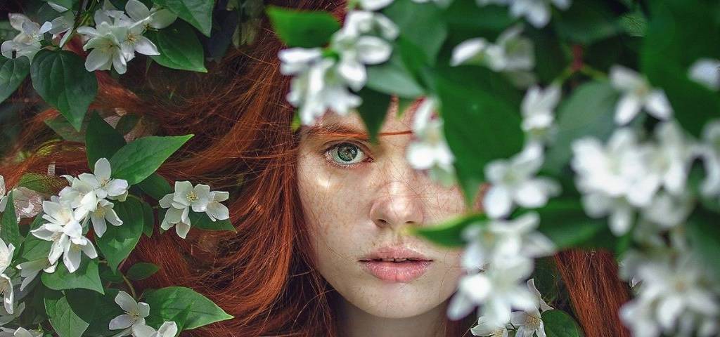 Jeune femme rousse apparaissant dans des feuilles vertes et des fleurs blanches