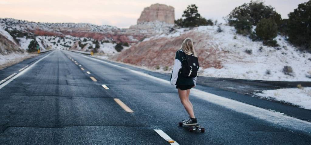 Jeune femme de dos faisant du skate sur une route