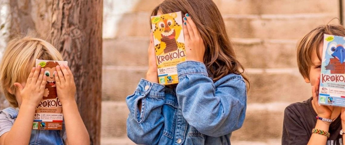Les tablettes Krokola sont faîtes à partir d’ingrédients simples et d’origine naturelle, sans additif, arôme ou conservateur. Jeunes enfants avec le visage caché par une tablette de chocolat Krokola