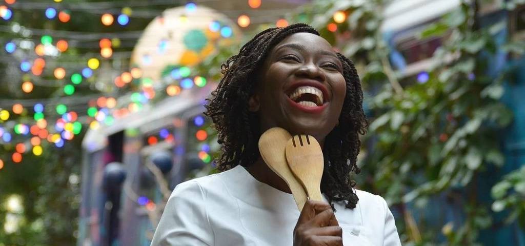 Femme noire avec des couverts à salade en bois, riant aux éclats