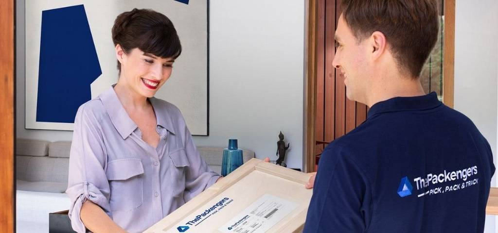 Femme recevant un colis, d'un livreur portant un t-shirt avec le le logo ThePackengers
