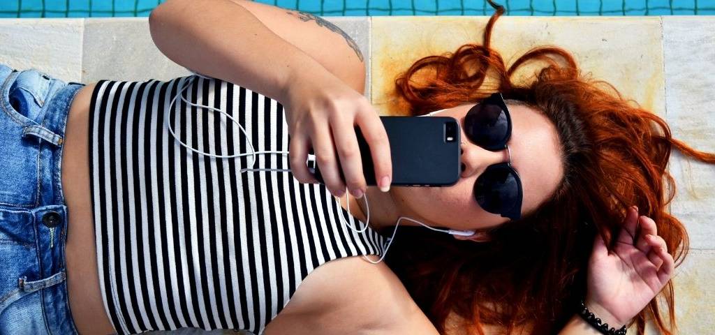 Jeune femme allongée au bord d'une piscine, elle regarde son téléphone