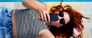 Jeune femme allongée au bord d'une piscine, elle regarde son téléphone