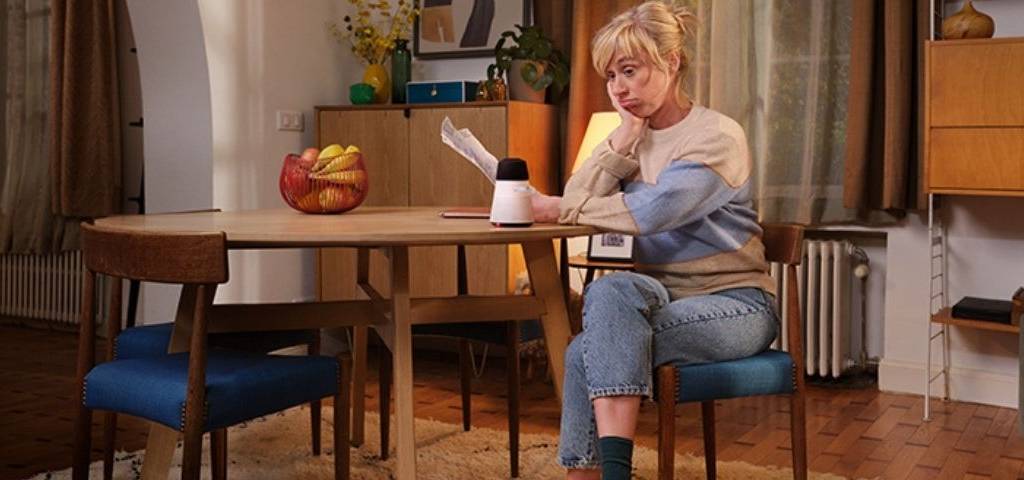 Une femme assise à table, elle a l'air perplexe, elle se pose une question. Nouvelle campagne Axa