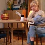 Une femme assise à table, elle a l'air perplexe, elle se pose une question. Nouvelle campagne Axa