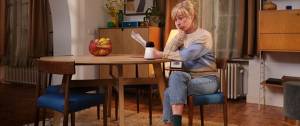Une femme assise à table, elle a l'air perplexe, elle se pose une question. Nouvelle campagne Axa