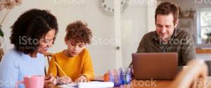 Papa travaillant sur son ordinateur pendant que la maman aide un enfant à faire ses devoirs