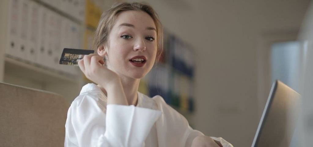 jeune fille devant un ordinateur avec une carte de crédit à la main