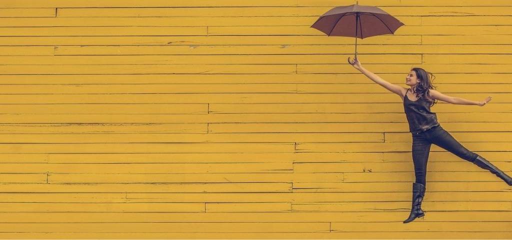 Jeune femme s'envolant en tanant un parapluie, sur un fond jaune