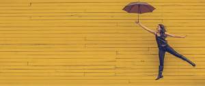 Jeune femme s'envolant en tanant un parapluie, sur un fond jaune