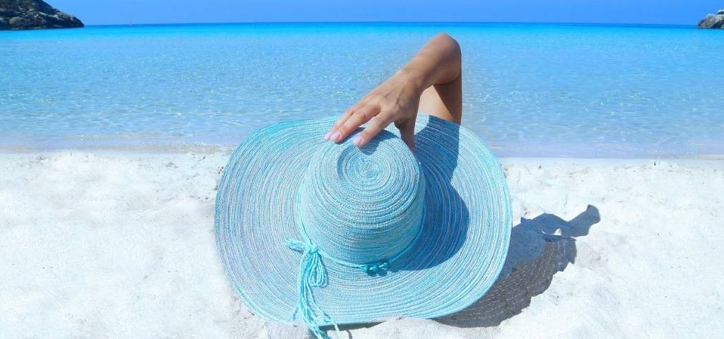 Femme allongée sur la plage, avec le visage caché derrière un chapeau de paille bleu