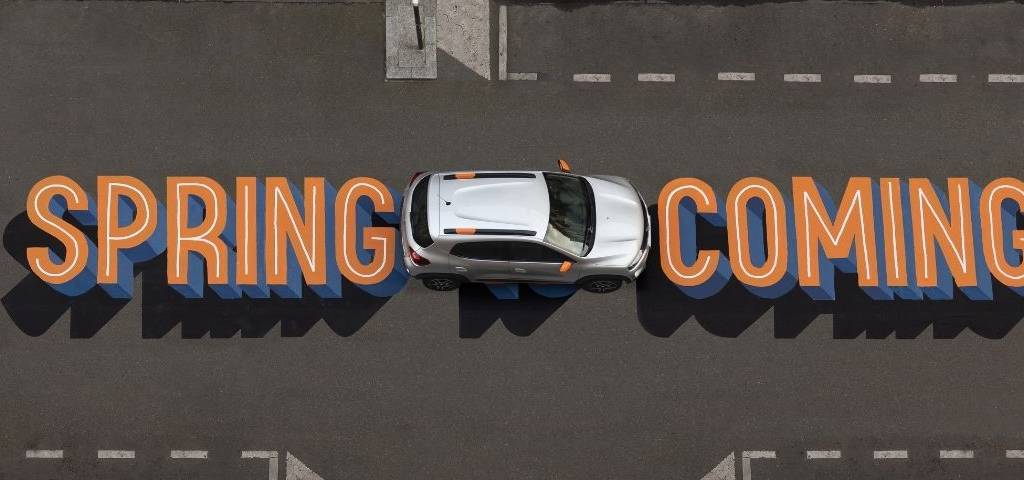 Voiture Dacia prise en hauteur avec le message  - Spring is coming -  inscrit sur la route en orange et bleu