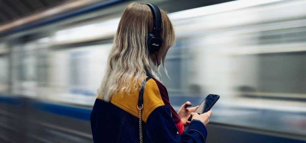 Une femme qui écoute du son au travers d'un casque de musique. Elle se trouve dans une station de métro