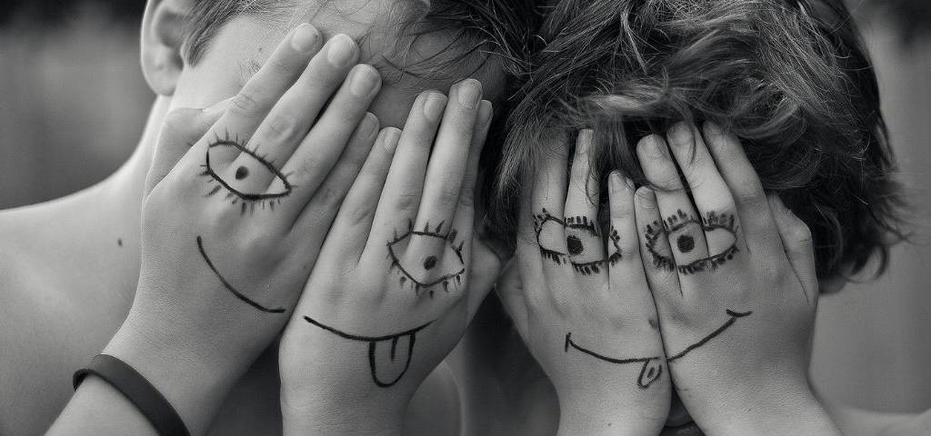 Deux enfants qui se cachent le visage avec leurs mains. Ils ont dessiné des smileys