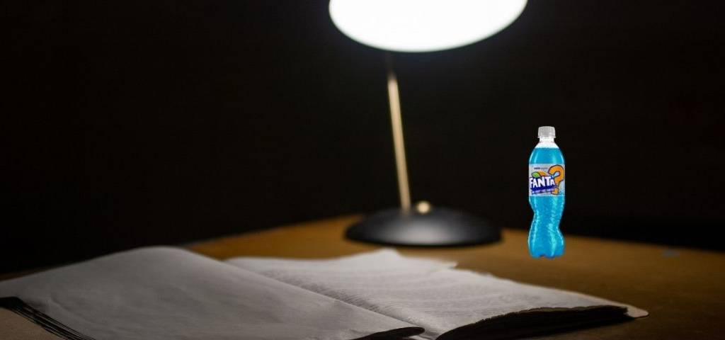 Un bureau avec une lampe, un cahier ouvert et une bouteille de Fanta