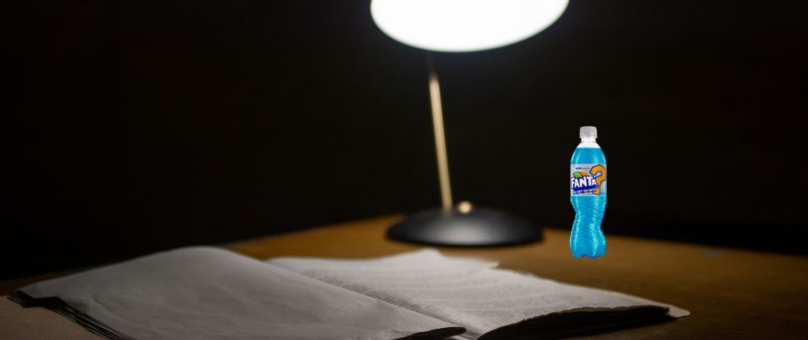 Fanta-saveur-bleu-céremonie-Fanta-Fun-Awards-créateurs-contenus-réseaux-sociaux Un bureau avec une lampe, un cahier ouvert et une bouteille de Fanta