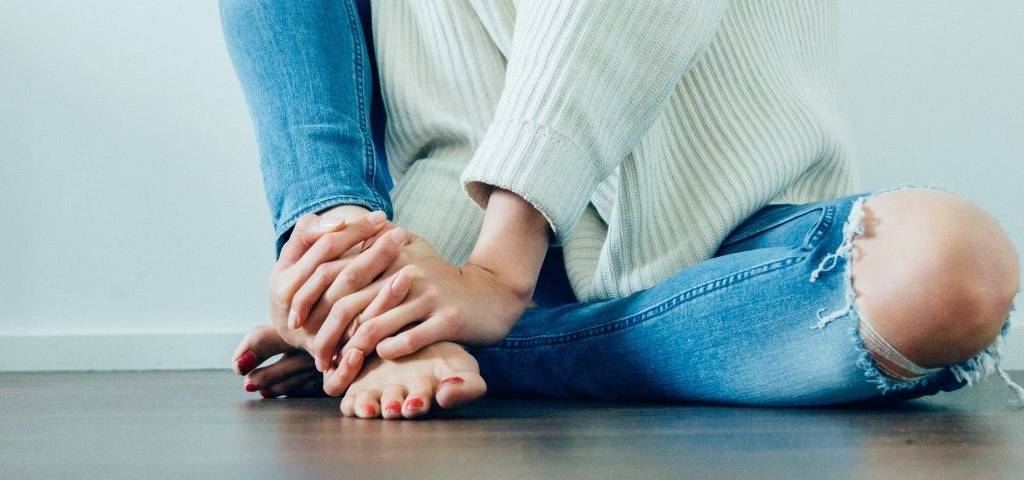 bas du corps d'une femme, assise par terre, qui serre tous ses doits autour de sa jambe