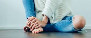 bas du corps d'une femme, assise par terre, qui serre tous ses doits autour de sa jambe