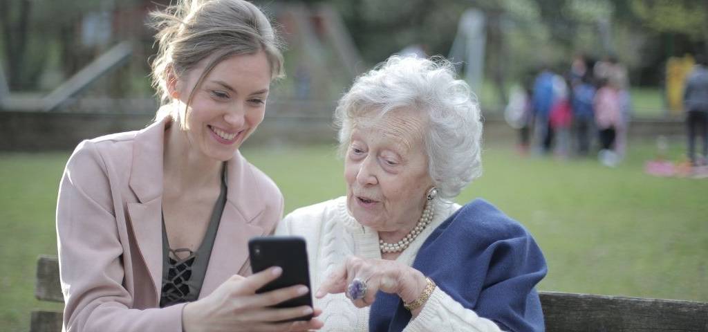 Jeune femme et personne âgées sur un banc avec un smartphone