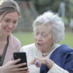 Jeune femme et personne âgées sur un banc avec un smartphone