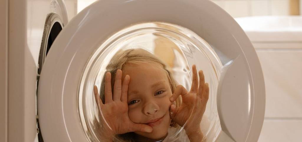Petite fille faisdant coucou derrière la vitre du hublot d'une machine à laver