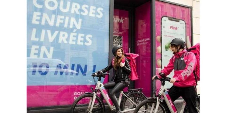 Deux personnes à vélo, avec une affiche :  - Flink, courses enfin livrées en 10 minutes - 