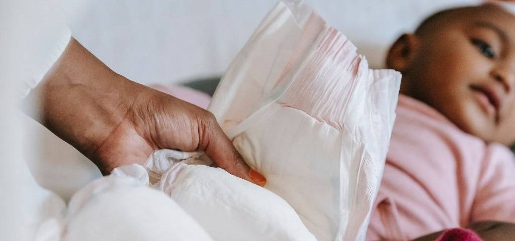 Femme tenant une couche dans ses mains avec en arrière plan un bébé allongé