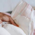 Femme tenant une couche dans ses mains avec en arrière plan un bébé allongé