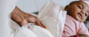 Femme tenant une couche dans ses mains avec en arrière plan un bébé allongé