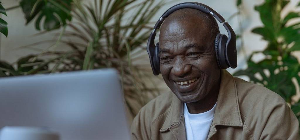 Homme avec un casque sur les oreilles, riant devant un ordinateur
