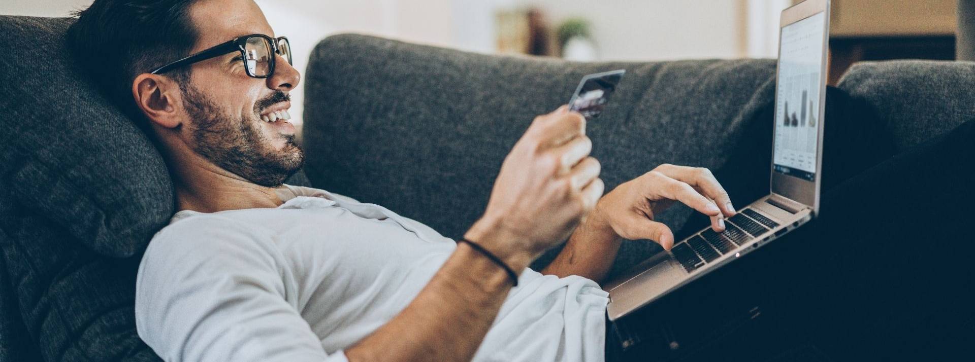 L’usage des ventes de produits sur Internet a largement été démocratisé pendant la pandémie Homme allongé sur un canapé devant un oridinateur avec une carte bancaire dans la main