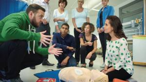 Homme formant une femme aux gestes de premier secours avec un mannequin au sol