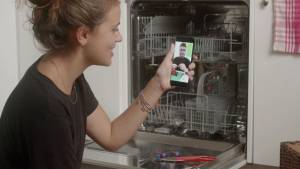 Femme avec un smartphone devant un lave-vaisselle