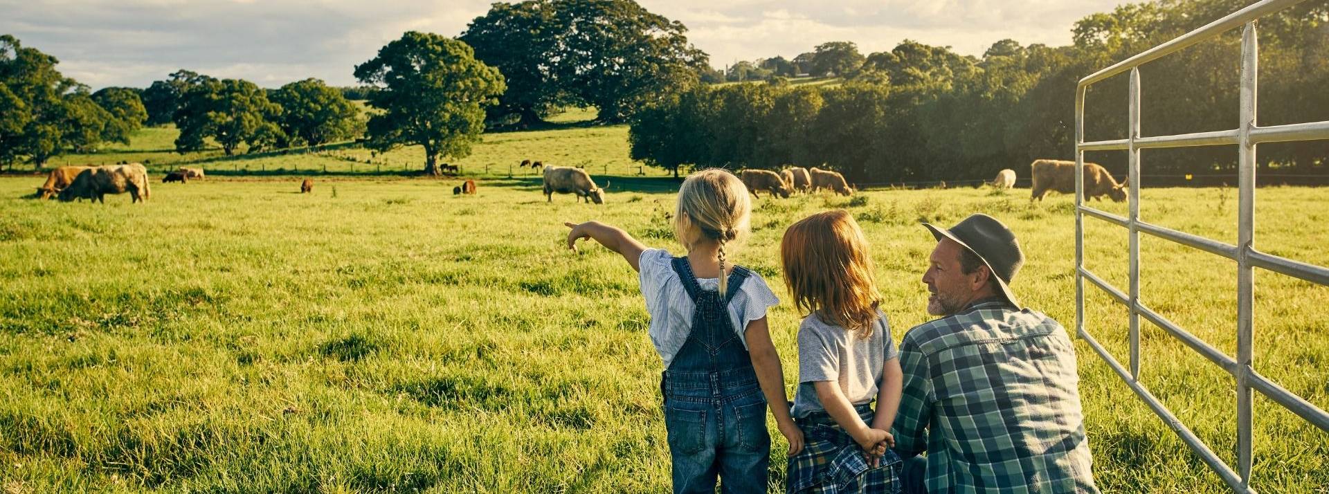 La nouvelle marque éthique Transition rejoint les rayons d'Auchan pour faciliter le passage au bio des agriculteurs en les rémunérant justement pendant la difficile période de conversion Homme accroupi dans un champ montrant des vaches à deux enfants