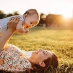 Maman portant son bébé au dessus delle allongée dans un pré