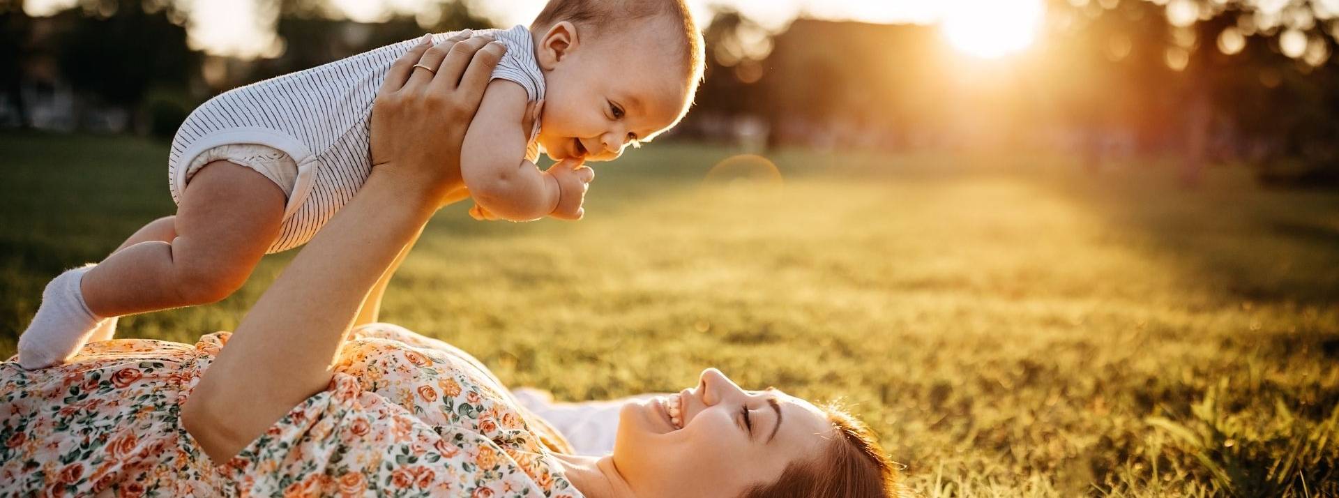 Babybio, marque française d'alimentation infantile bio dévoile sa nouvelle campagne Maman portant son bébé au dessus delle allongée dans un pré