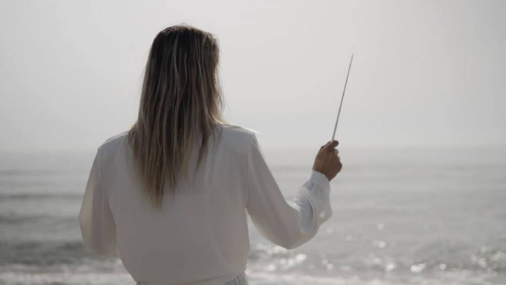 Femme en position de chef d'orchestre devant l'océan