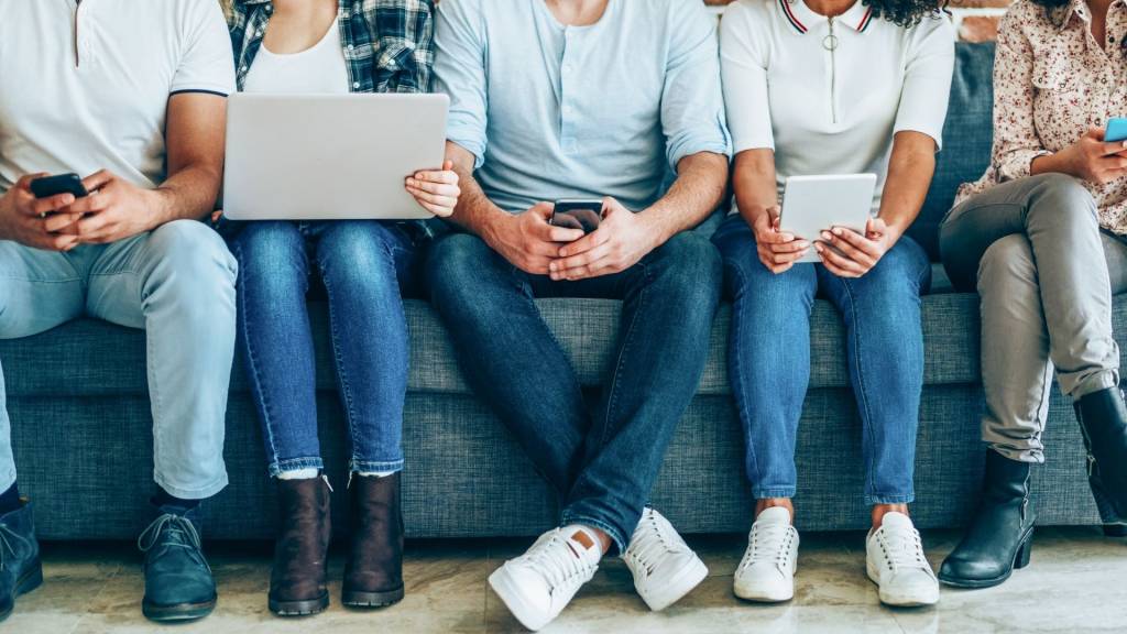 Personnes assisent sur un canapé devant des écrans de téléphone, tablette ou ordinateur