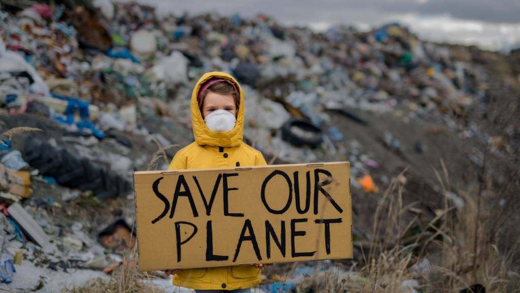 Jeune fille avec un masque et devant un tas de déchet tenant une pancarte : Save our Planet