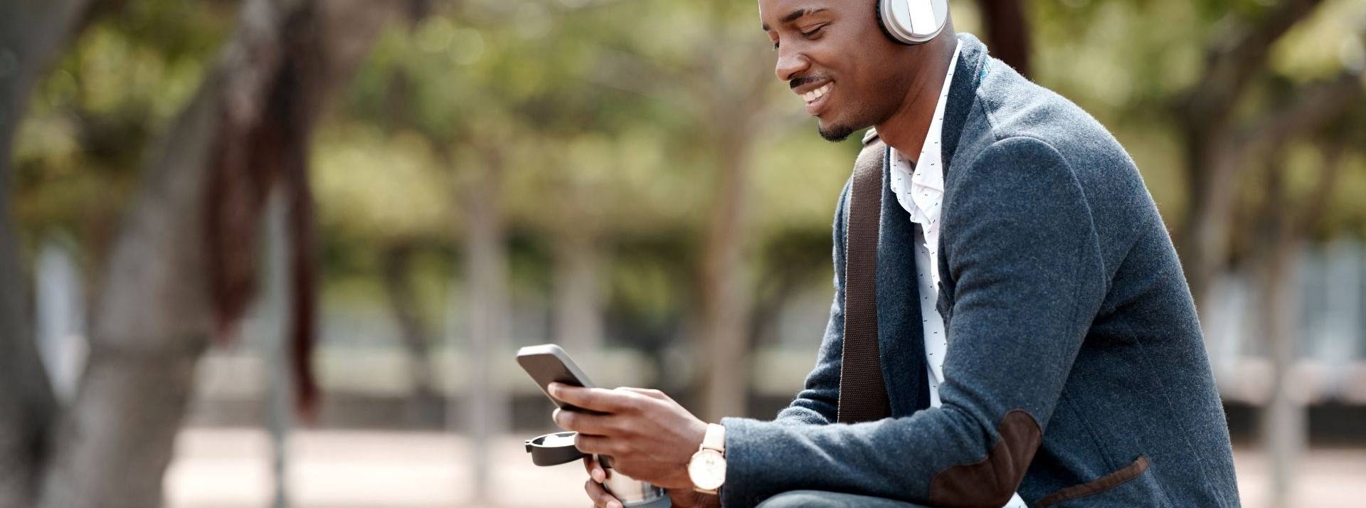 L'ESSCA lance sa chaine de podcasts, une innovation pédogoqique homme assis sur un banc avec un casque sur les oreilles et un smartphone dans la main