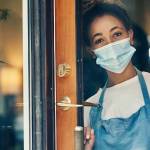 Femme à la porte de sa boutique avec un écriteau "open"
