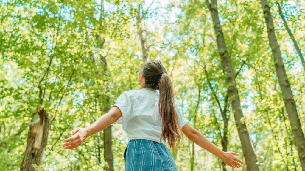 Jeune fille levant les bras devant une forêt