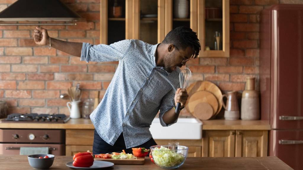 Homme dan sa cuisine chantant avec un fouet en guise de micro