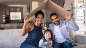 une famille assise sur un canapé tenant un carton qui fait office de toit au dessus de leur tête