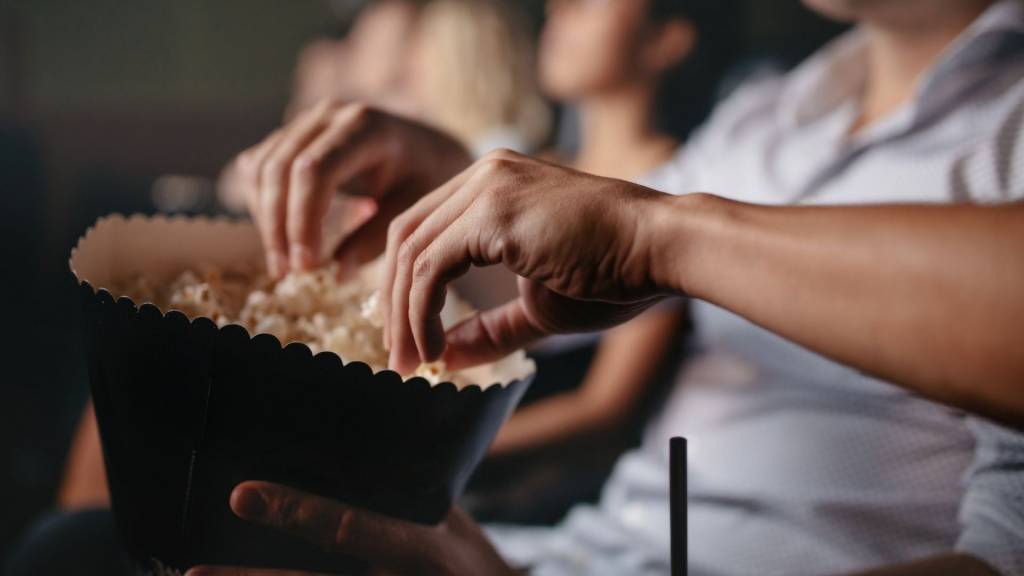 Des mains tiennent un sachet de popcorn dans une salle de cinéma.
