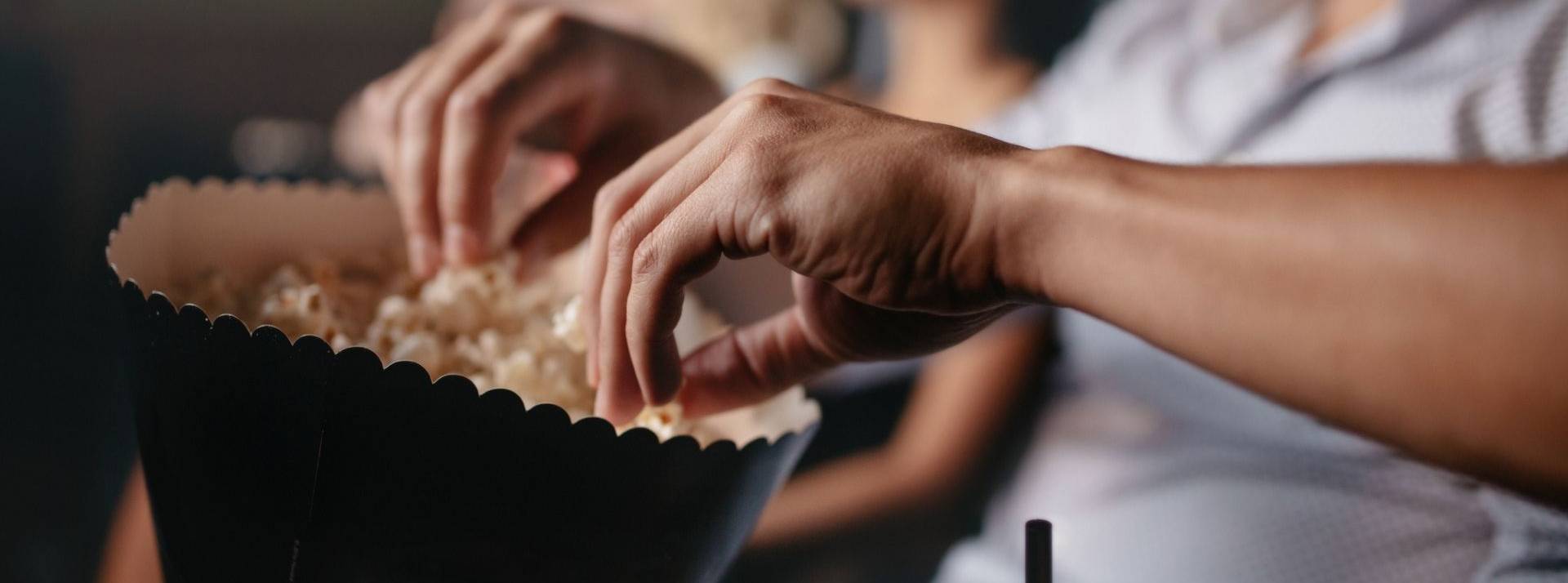 AMC Entertainment étend son entreprise vers l’industrie du popcorn. Des mains tiennent un sachet de popcorn dans une salle de cinéma.