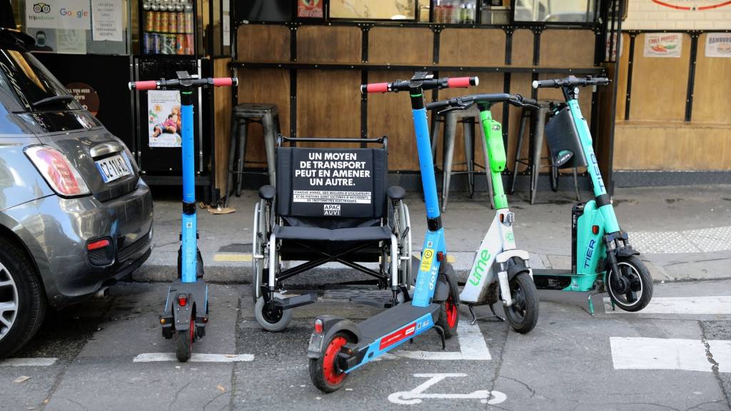 Fauteuil handicapé sur une place réservé, entouré de trottinettes