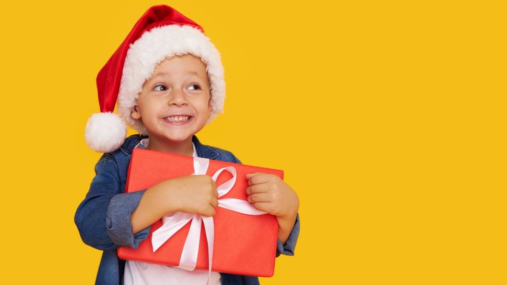 Enfant avec un chapeau de père noel tenant dans ses bras un cadeau
